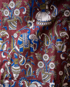 A close-up of a patterned textile featuring a traditional Indian block print design with a blue elephant, white flowers, and ornate paisley motifs on a deep maroon background.