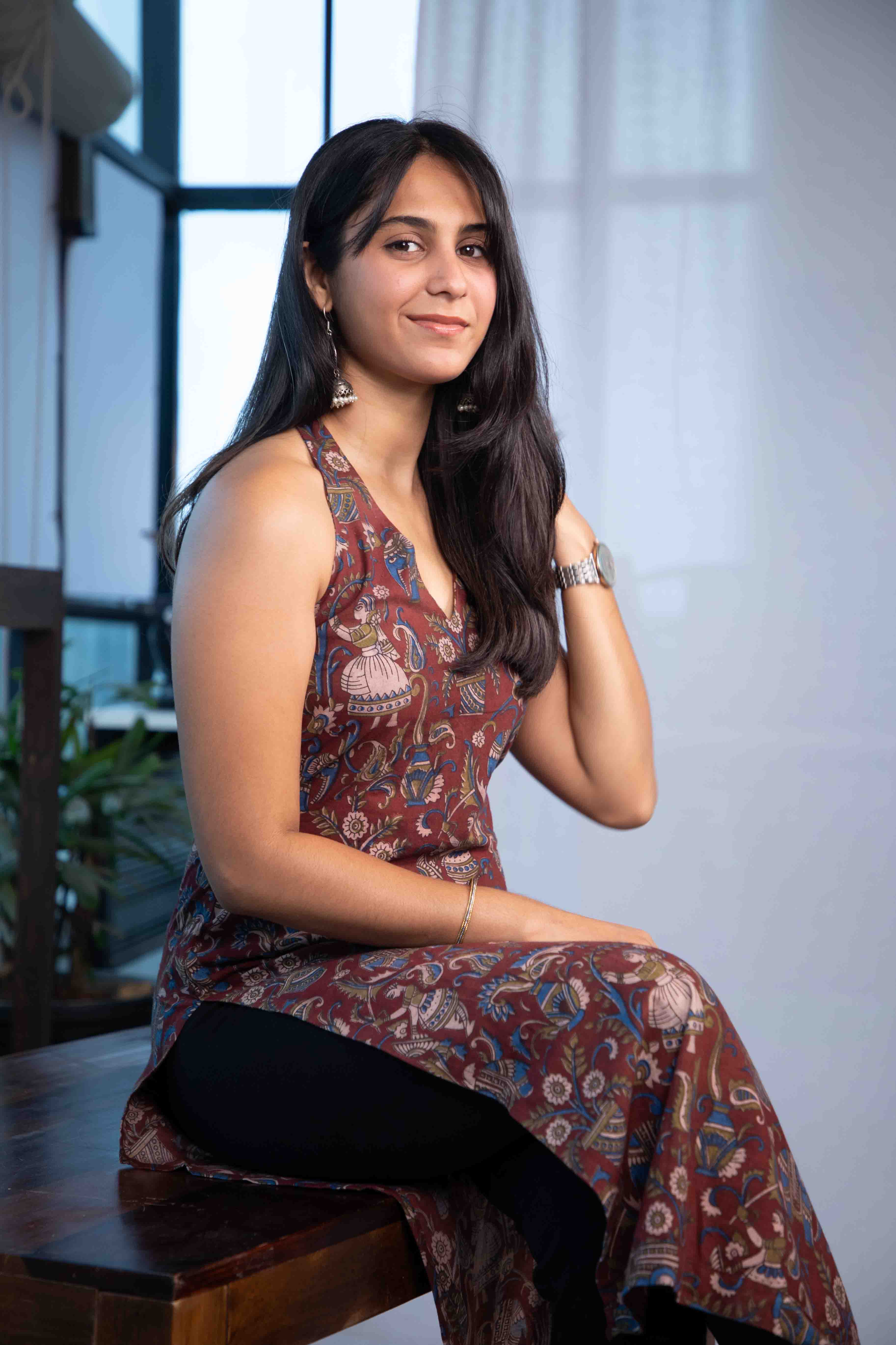 Woman wearing a patterned dress sitting indoors with a blurred background