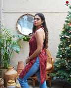 Woman in a red patterned top and blue jeans standing in front of a Christmas tree and plants.